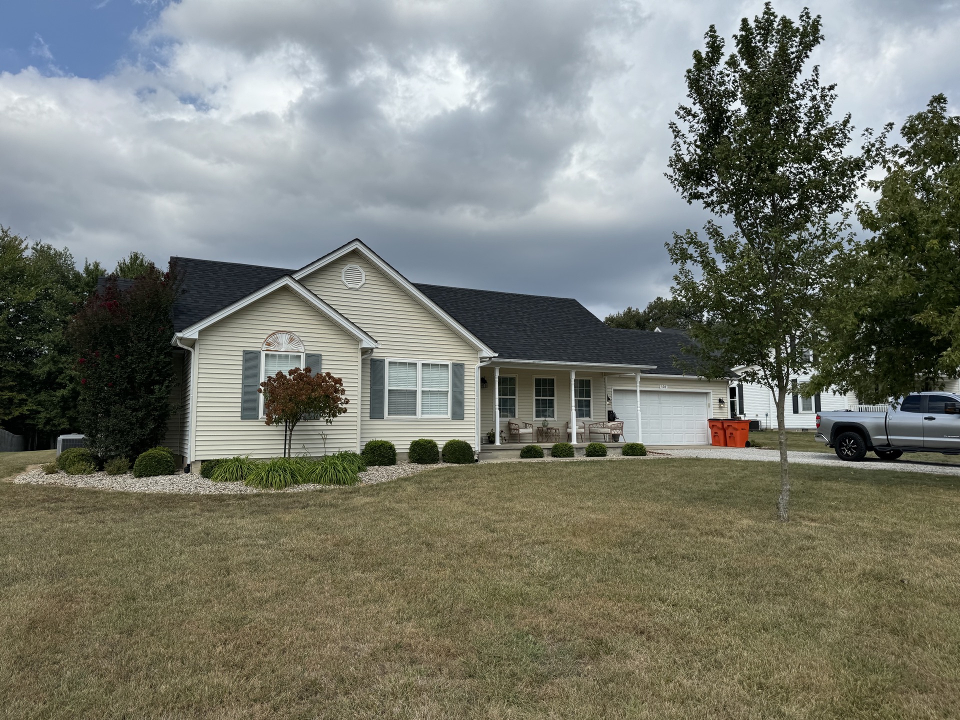 Cream siding ranch home with a new dark shingle roof, front porch, and two-car garage.
