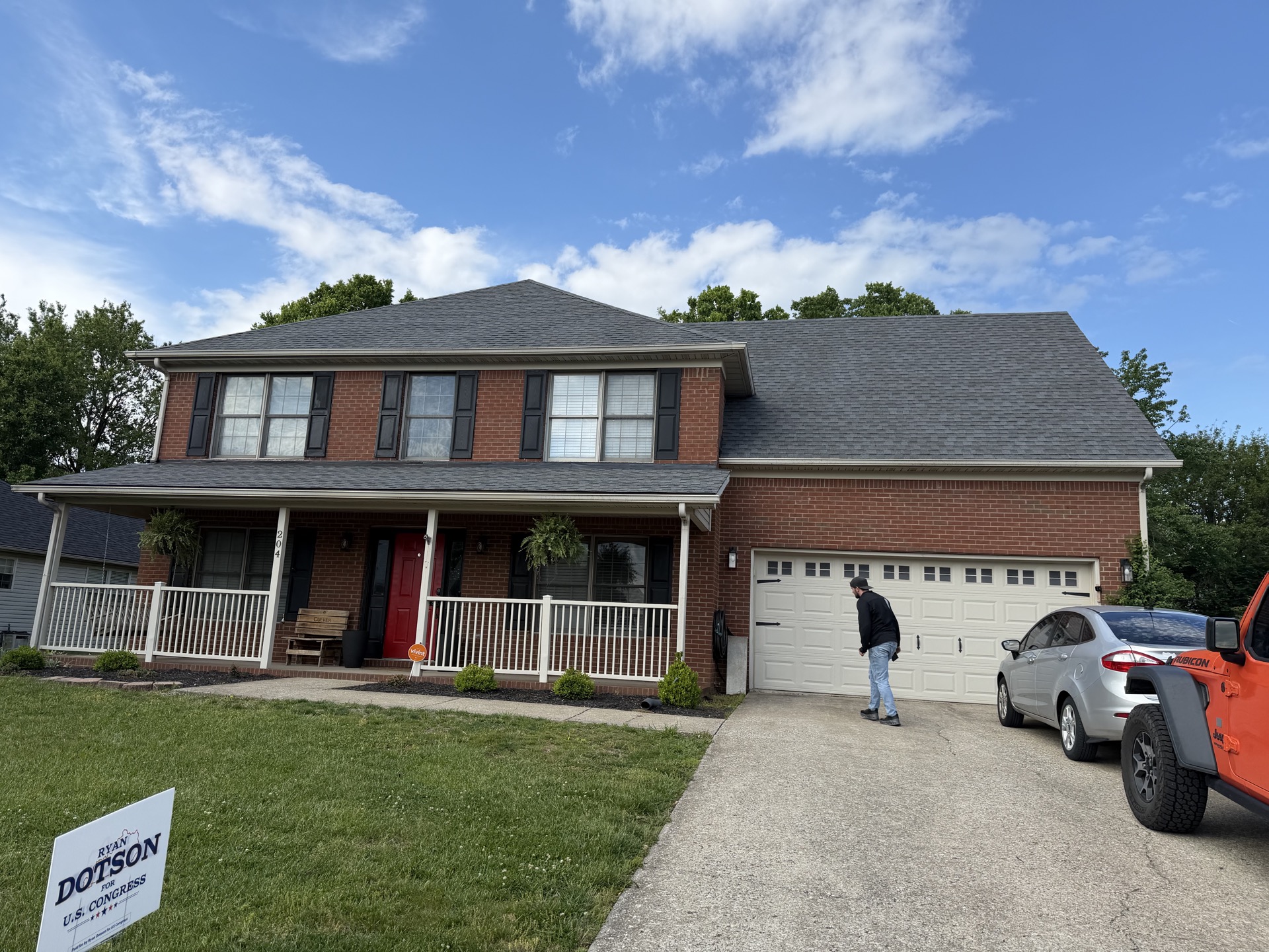 Two-story red brick home with a new dark architectural shingle roof, front porch, and attached garage.